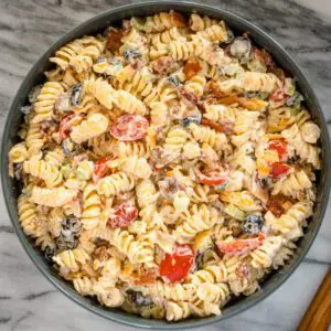 A serving bowl of ranch pasta salad with bacon, tomatoes, olives, and more