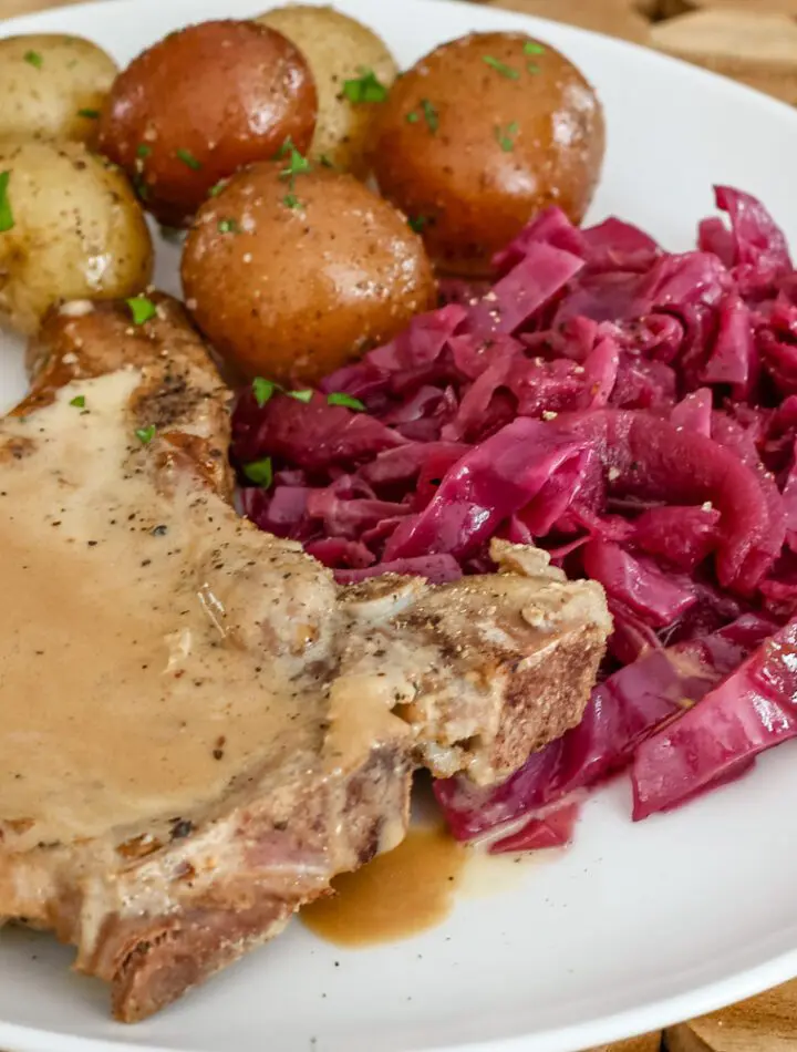 braised red cabbage is shown with a pork chop and baby potatoes on a plate