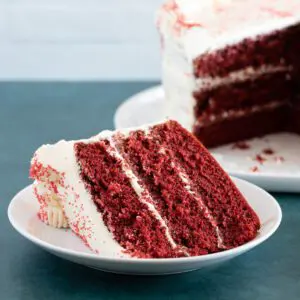 A slice of red velvet cake on a plate with cream cheese frosting