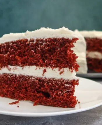 red velvet cake slice on a plate with the larger cake in the background