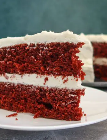 red velvet cake slice on a plate with the larger cake in the background