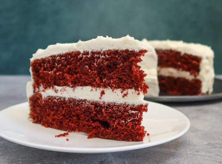 red velvet cake slice on a plate with the larger cake in the background