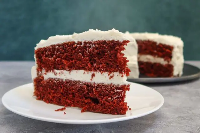 red velvet cake slice on a plate with the larger cake in the background