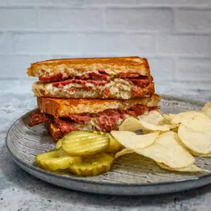 a reuben sandwich on a luncheon plate with chips and pickles