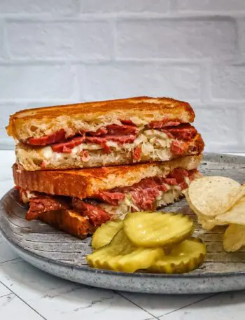 reuben sandwich on a plate with chips and pickles