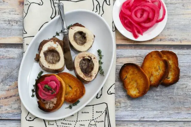 roasted bone marrow on an appetizer plate with pickled onions and crostini