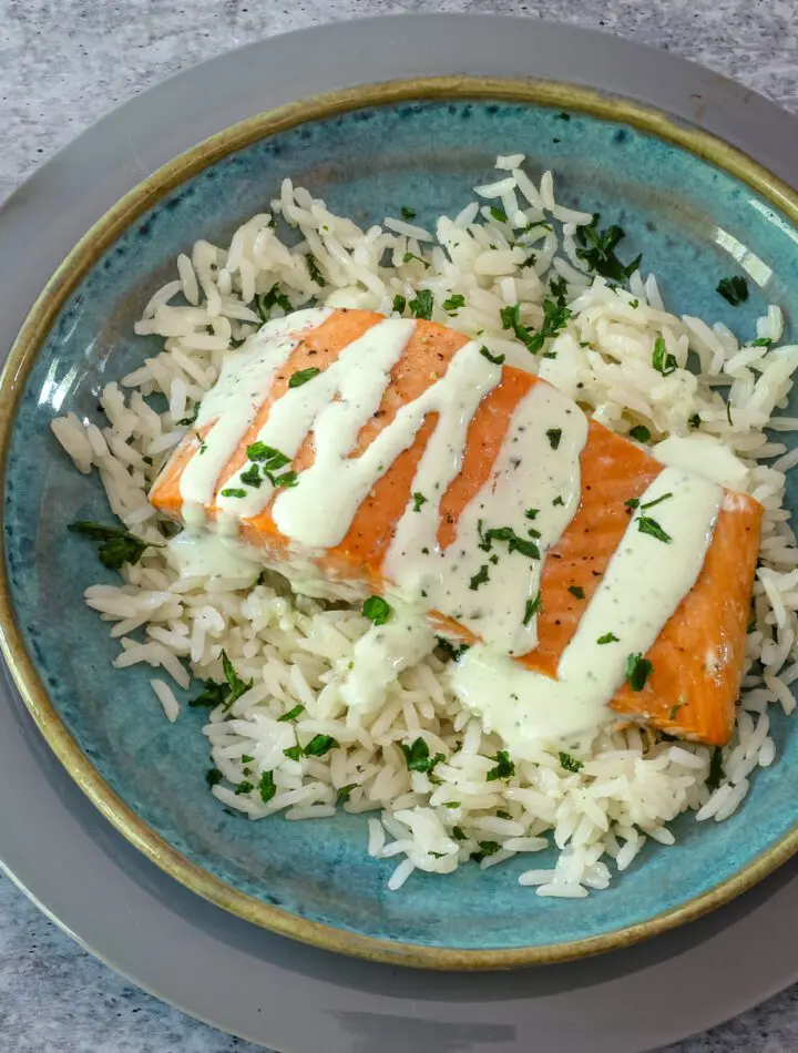 a salmon fillet on a bed of rice with a drizzle of basil mayonnaise.