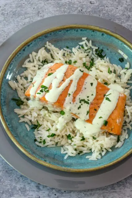 a salmon fillet on a bed of rice with a drizzle of basil mayonnaise.