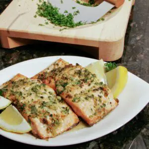 baked salmon fillets with lemon, garlic, and parsley on a plate with lemon wedges