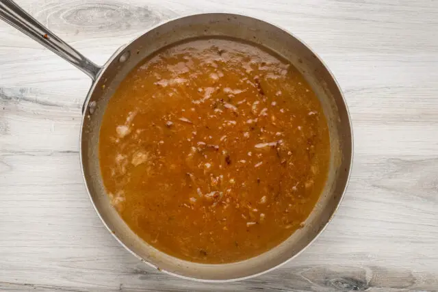 Sauce made with chicken broth and onions is simmering for smothered pork chops.