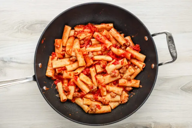 The rigatoni pasta is added to the sausage ragu in the pan.