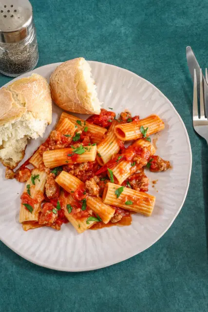 Overhead shot of a plate of rigatoni with a bright and flavorful sausage ragu made with Italian sausage, hand-crushed tomatoes, garlic, and onions.