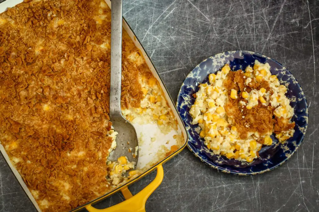 Scalloped corn casserole in a baking dish with some on a small plate on the side.