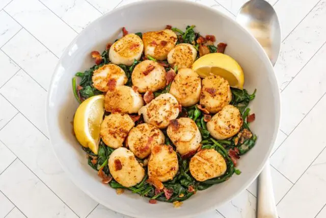 seared scallops in a serving dish on spinach with bacon