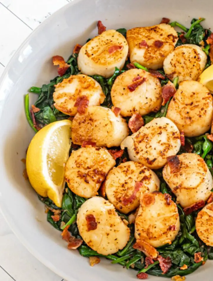 scallops on a bed of spinach with lemon wedges and bits of bacon