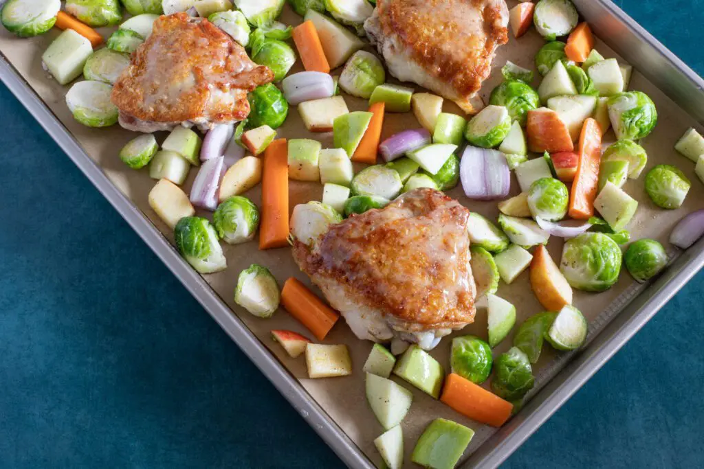 sheet pan with chicken thighs and brussels sprouts and apples, ready to roast.