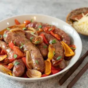 sheet pan sausages and peppers in a serving bowl with some parmesan cheese on the side