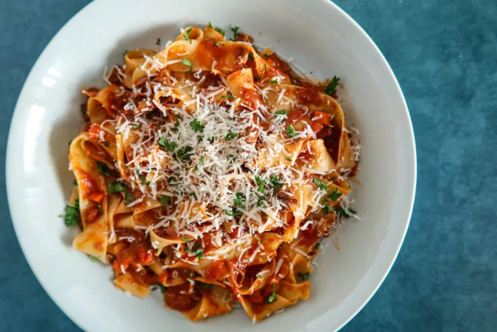 a bowl of short rib bolognese with pasta and parmesan cheese