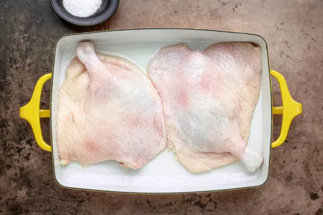 Preparing confit duck legs in the baking pan, seasoned with salt and ready to bake.