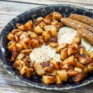 A plate of skillet home fries with sausages and eggs