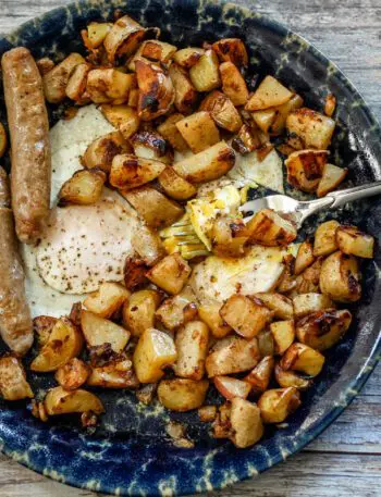 skillet home fries shown in a plate with eggs and sausages