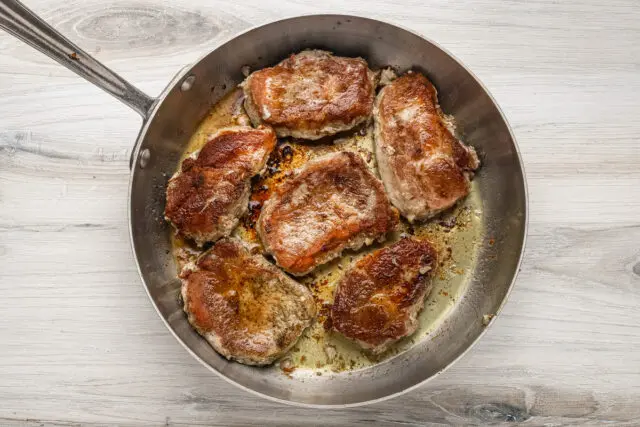 Pork chops are seared in the skillet for a smothered pork chop recipe.