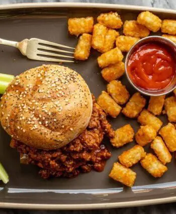 sloppy joe sandwich with tater tots and ketchup on the side.