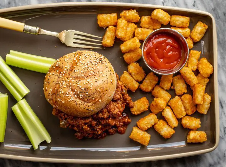 sloppy joe sandwich with tater tots and ketchup on the side.