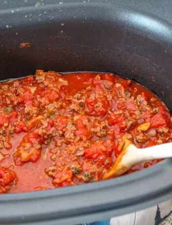 slow cooker bolognese sauce in the slow cooker with a wooden spoon