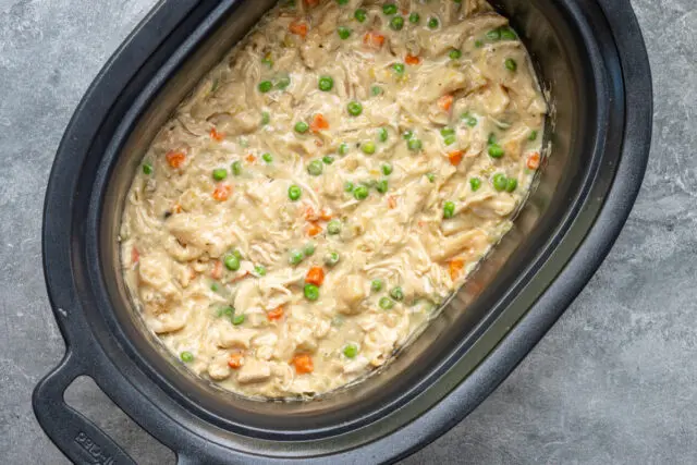 The slow cooker with finished chicken and dumplings made with refrigerated biscuits and peas and carrots.