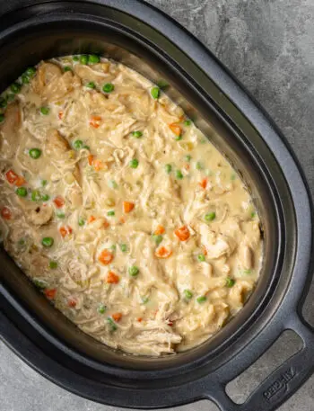 The slow cooker with finished chicken and dumplings made with refrigerated biscuits and peas and carrots.