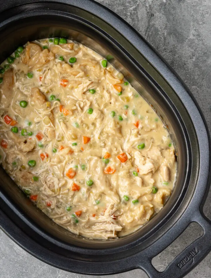 The slow cooker with finished chicken and dumplings made with refrigerated biscuits and peas and carrots.