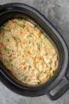 The slow cooker with finished chicken and dumplings made with refrigerated biscuits and peas and carrots.