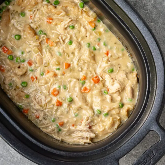 The slow cooker with finished chicken and dumplings made with refrigerated biscuits and peas and carrots.