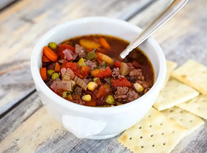 slow cooker hamburger soup in a bowl with crackers on the side.