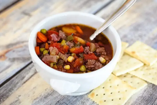 slow cooker hamburger soup in a bowl with crackers on the side.