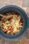 Slow cooker cooked kielbasa with apples, cabbage, onions, and tangy sauce, shown in the crock pot with a wooden spoon.