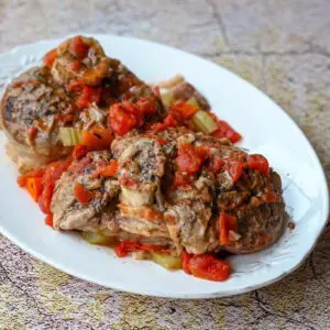 a platter with osso buco with tomatoes and diced vegetables