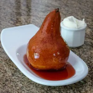 a poached pear with wine sauce on a serving plate