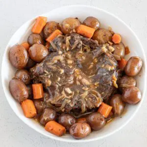 serving dish with pot roast surrounded by vegetables and gravy