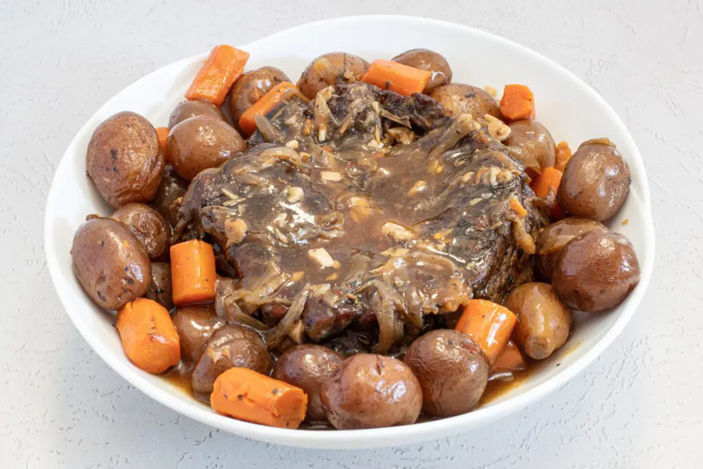 slow cooker pot roast in a serving dish with potatoes, carrots, and gravy.