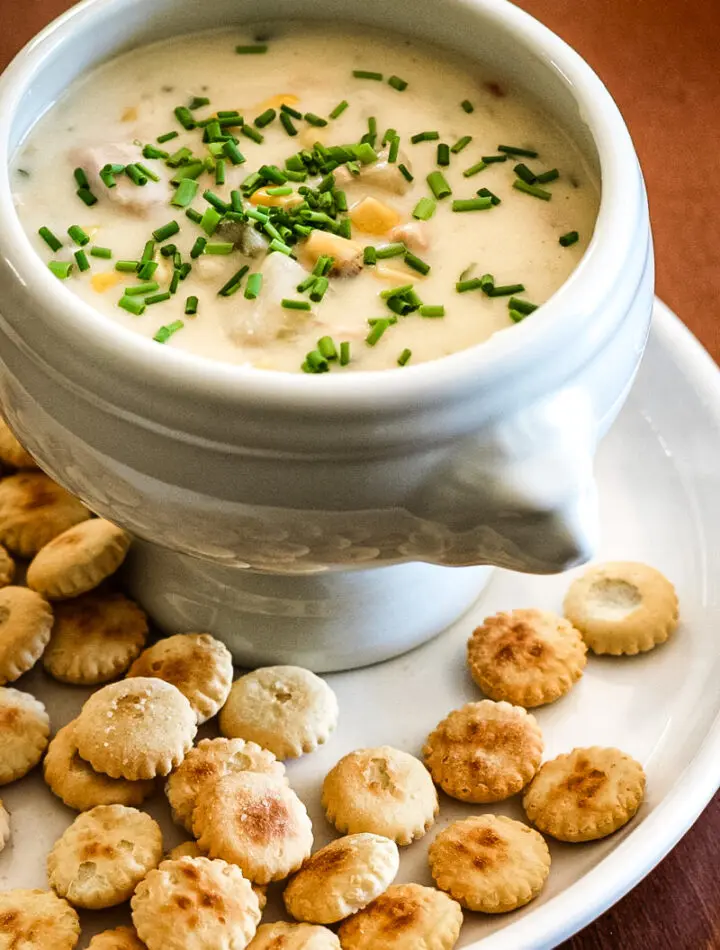 A bowl of tuna and corn chowder with oyster crackers on the plate.