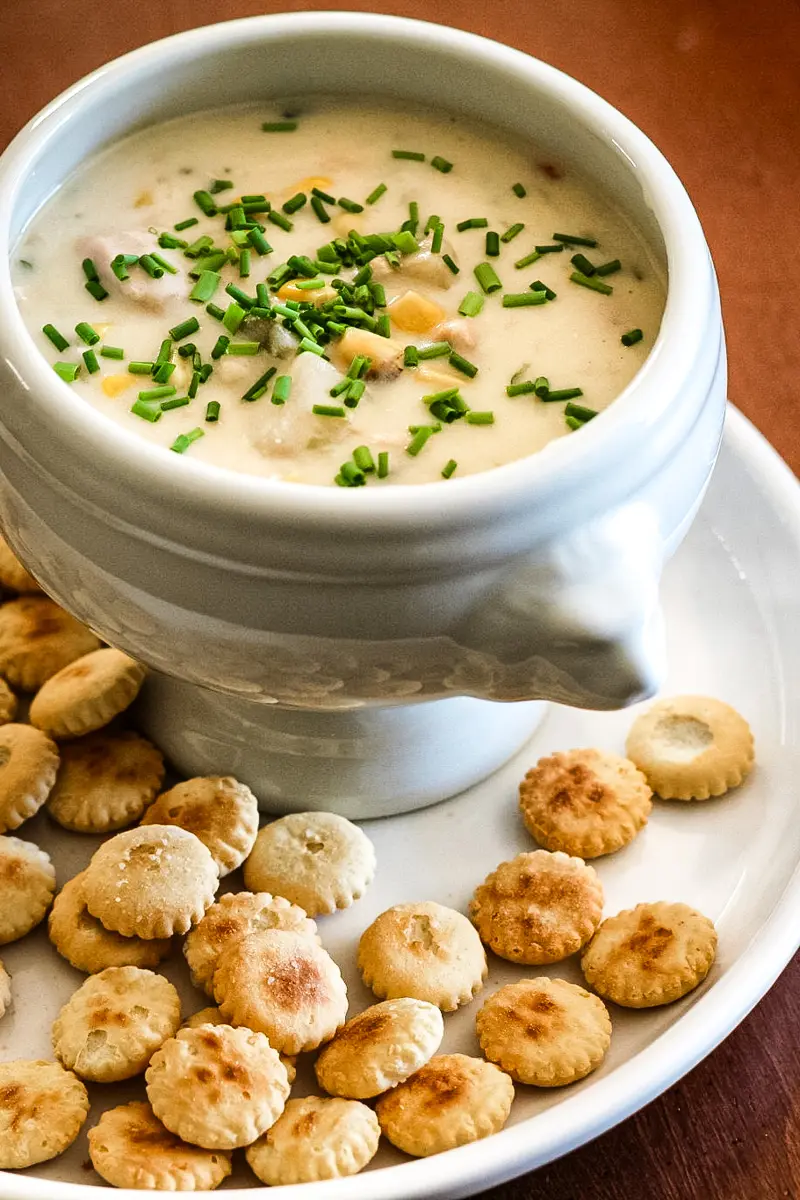 A bowl of tuna and corn chowder with oyster crackers on the plate.