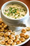 A bowl of tuna and corn chowder with oyster crackers on the plate.