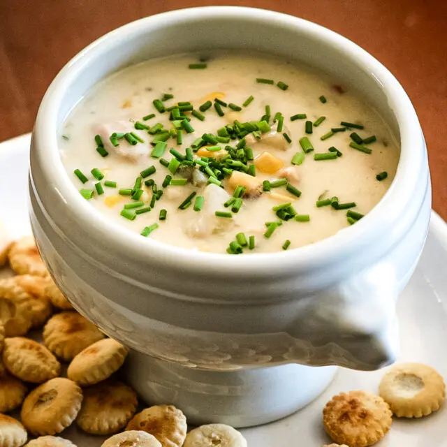 A bowl of tuna and corn chowder with oyster crackers on the plate.