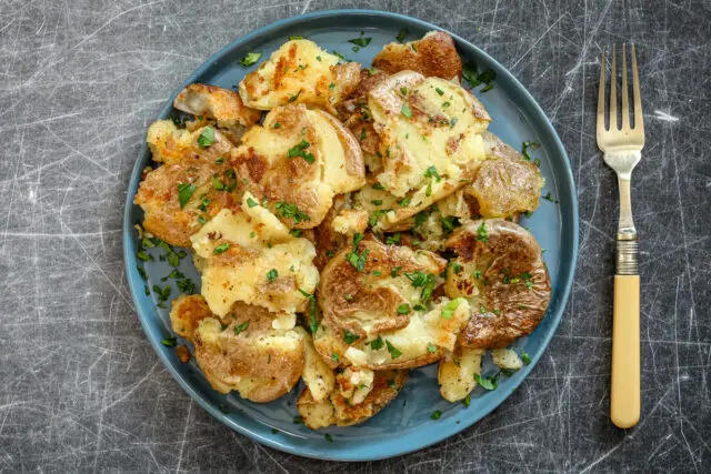 Fried smashed potatoes on a plate with parsley garnish.