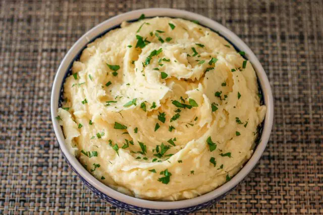 smoked cheddar mashed potatoes garnished with parsley in a serving bowl