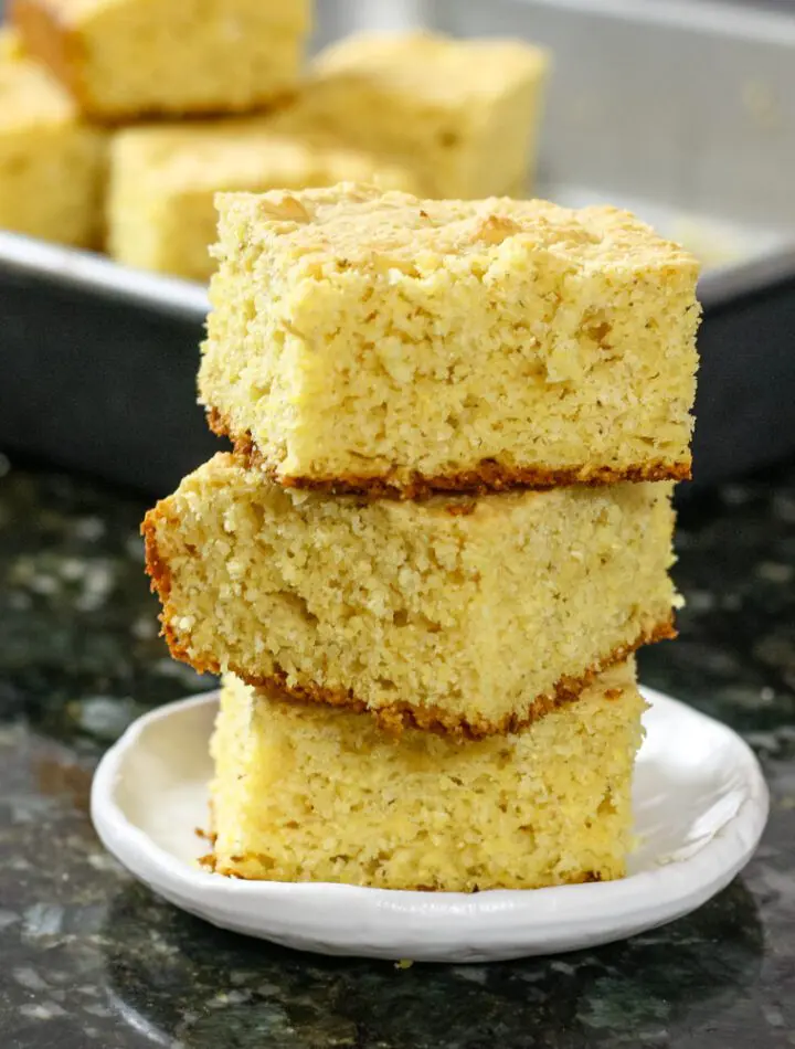 sour cream cornbread squares stacked with the pan in the background