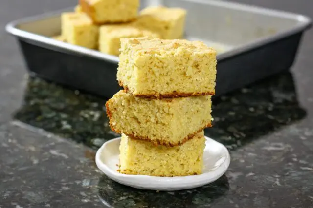 sour cream cornbread squares stacked with the pan in the background