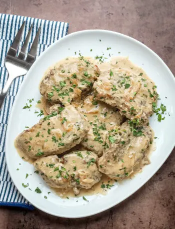 Smothered pork chops on a serving platter with parsley garnish.